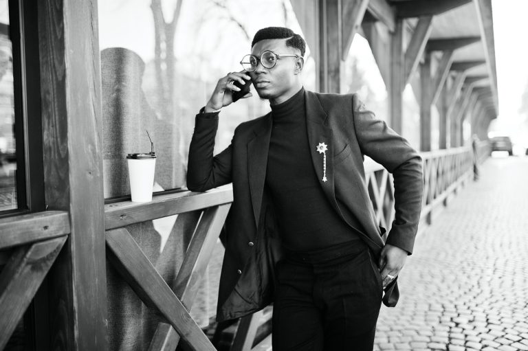 Thoughtful Man on Phone Call A man in formal attire talks on his smartphone while leaning against a wooden structure.