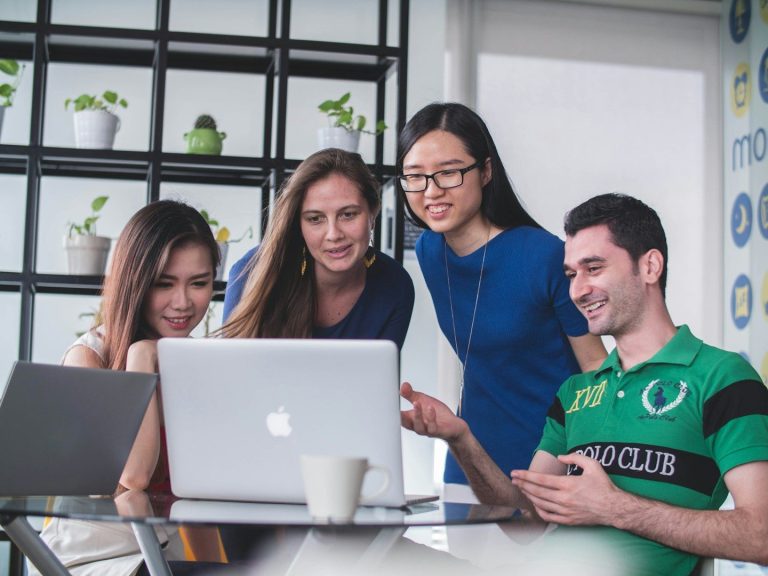 Three woman and man looking at one computer screen smiling
