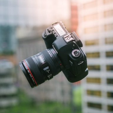 Floating Camera A DSLR camera with a large lens, floating above a cityscape background.