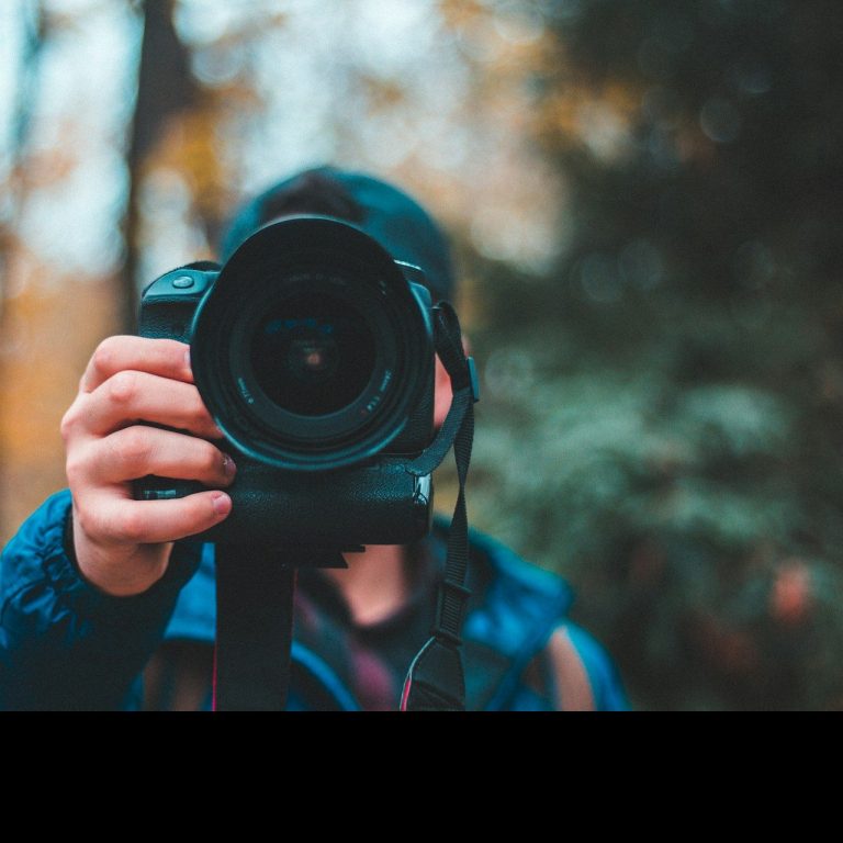 Camera man Person holding a camera, capturing a photo amidst autumn foliage.